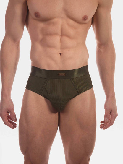 A close-up of a male model wearing low-rise, ribbed olive green briefs against a plain white studio background.