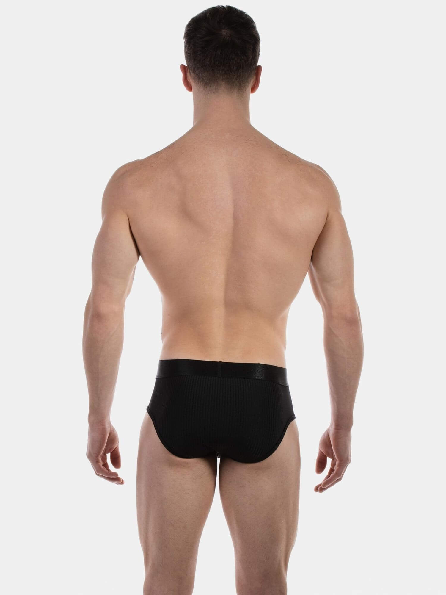 Rear view of a muscular man wearing black men's briefs against a light gray studio background.