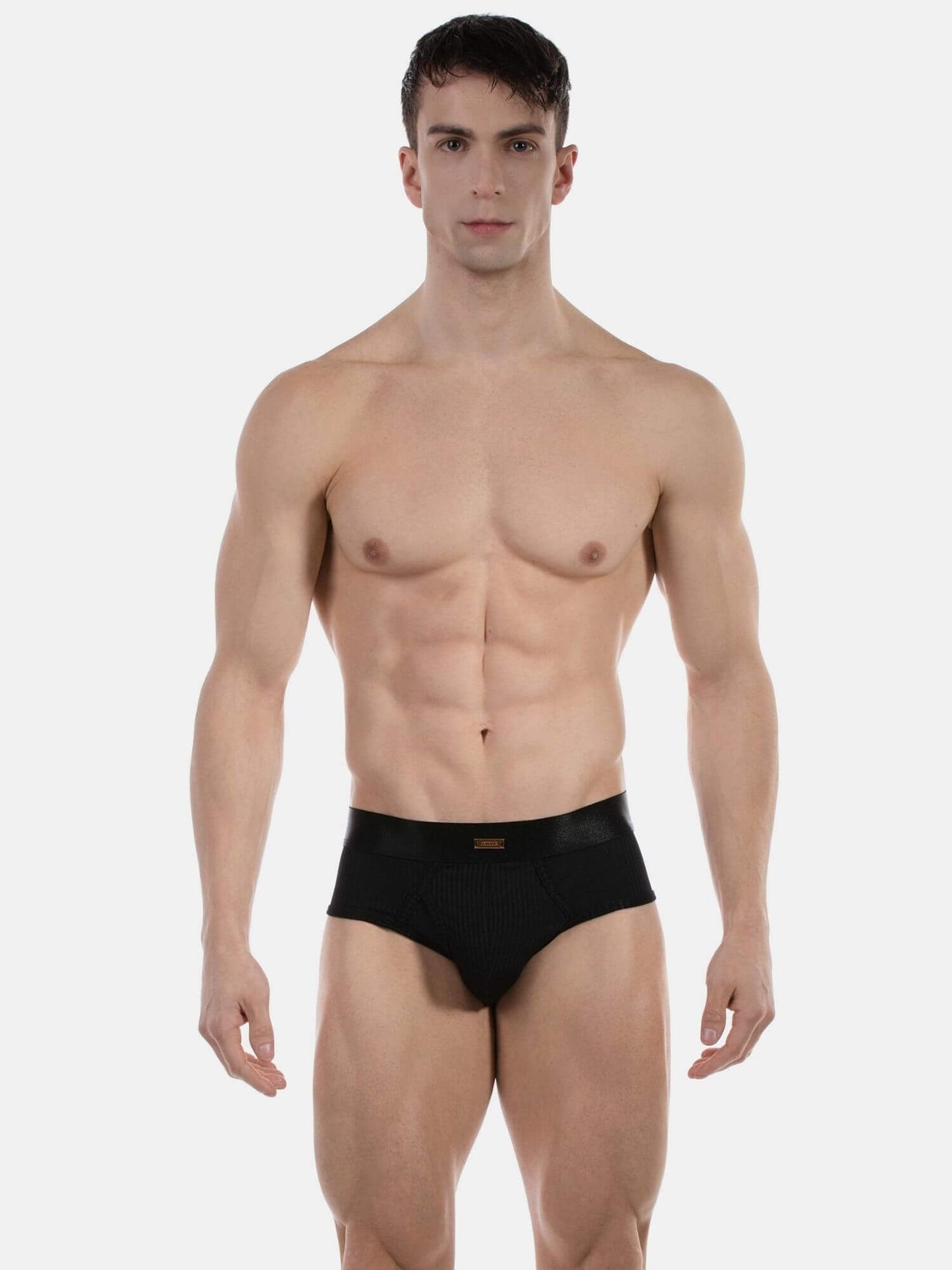 A muscular male model wearing black briefs against a plain light gray studio background.