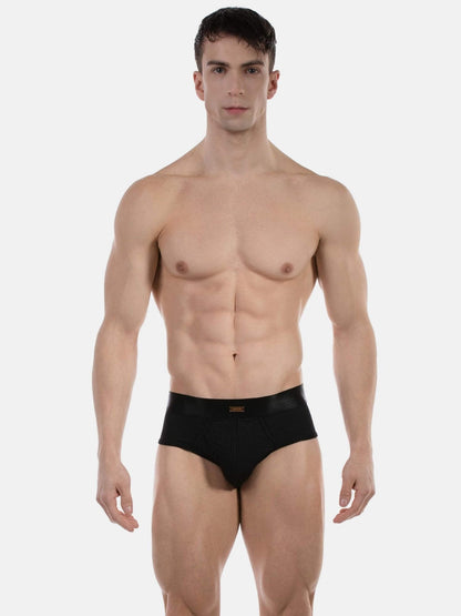 A muscular male model wearing black briefs against a plain light gray studio background.