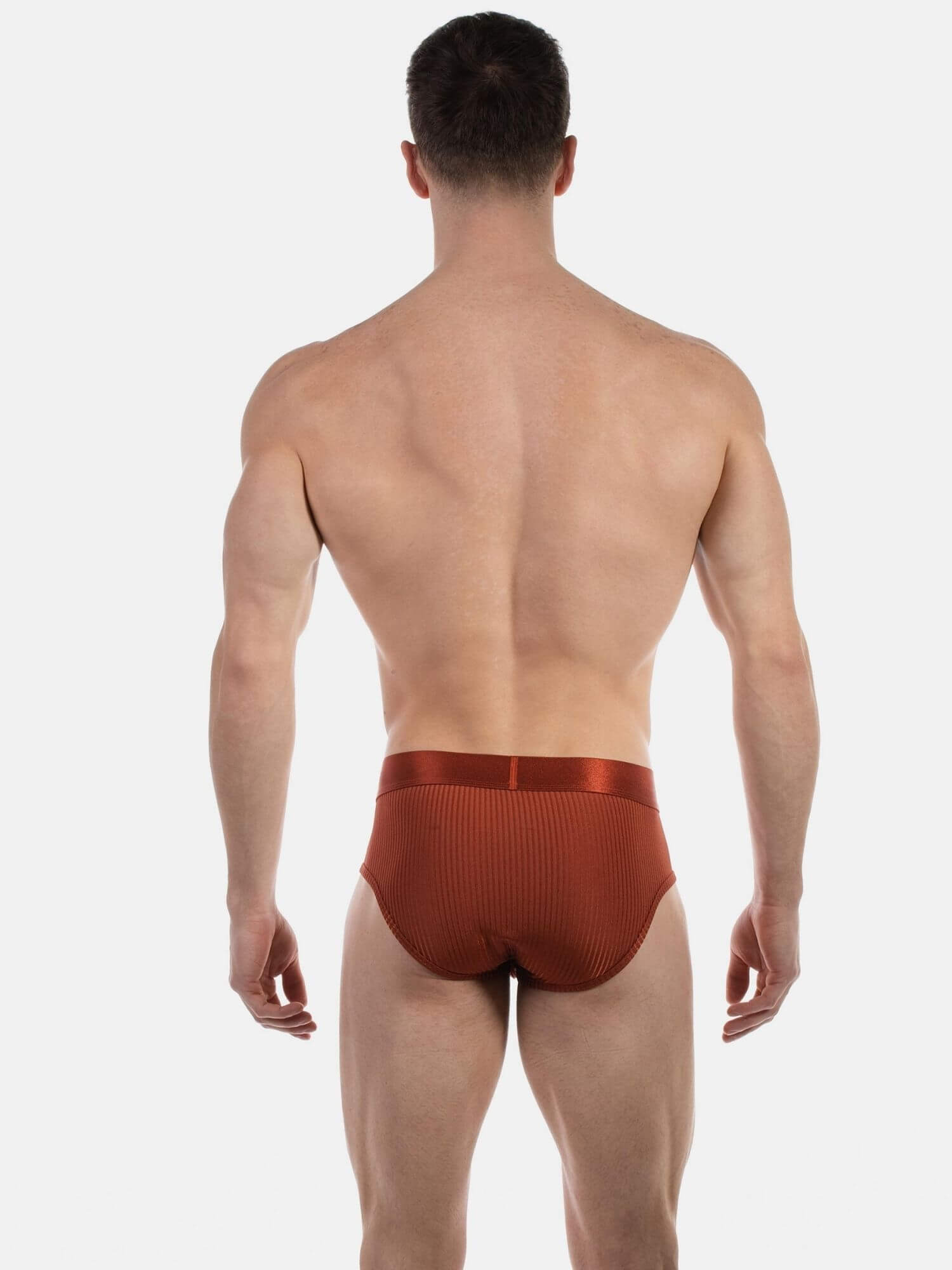 A man viewed from the back wearing ribbed brown underwear, standing against a light gray studio background.