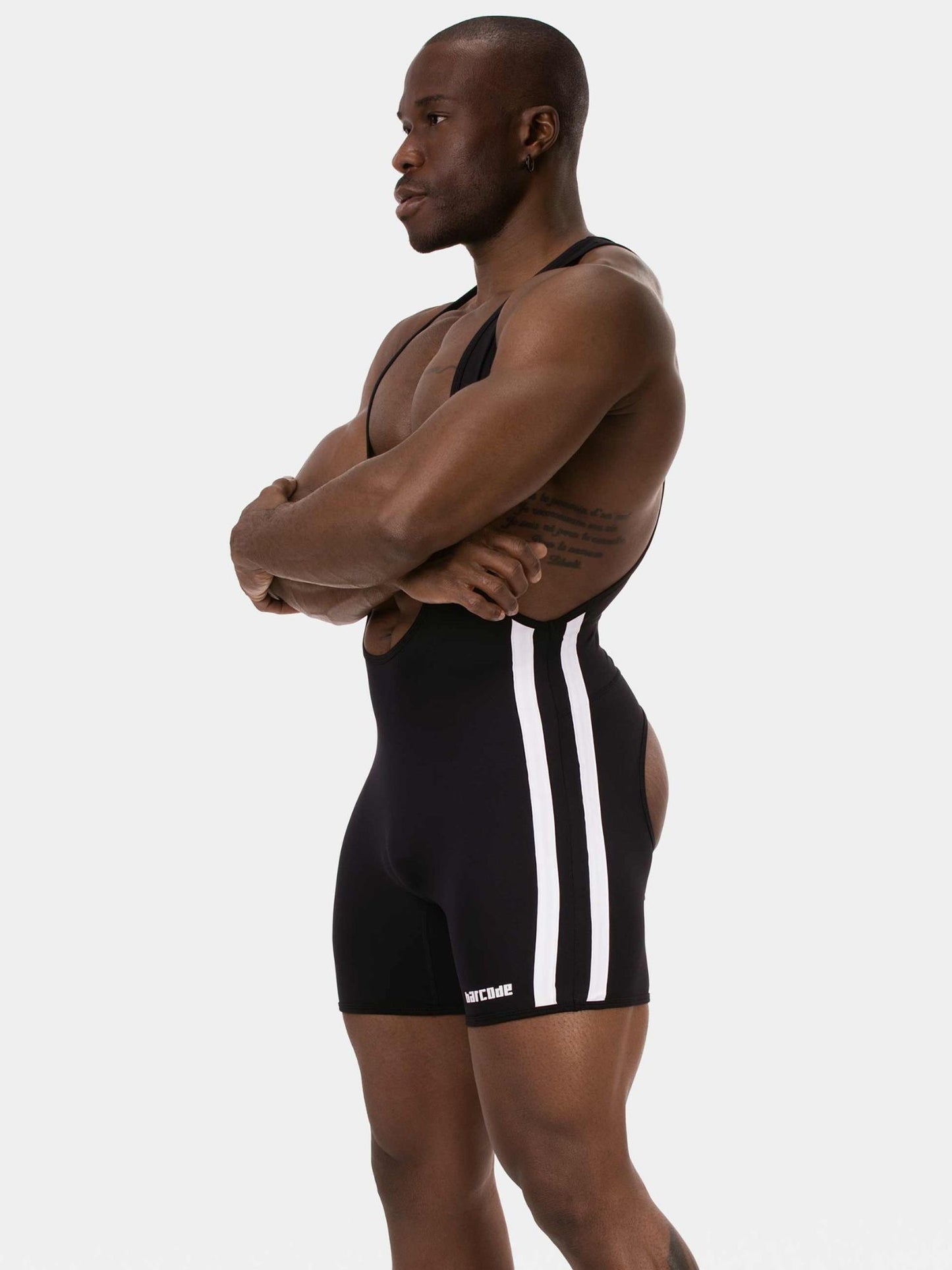 A muscular man in profile wearing a black athletic singlet with three white vertical stripes down the side, posed against a light gray studio background.