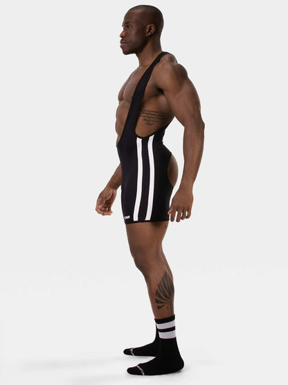 A muscular man in profile wearing a black athletic singlet with three white vertical stripes down the side, paired with black crew socks, against a plain light gray studio background.