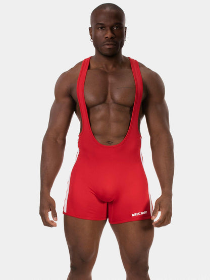 A muscular man modeling a bright red athletic singlet with wide shoulder straps and fitted shorts, standing against a light gray studio background. The brand name is visible in white on the lower right leg of the singlet.