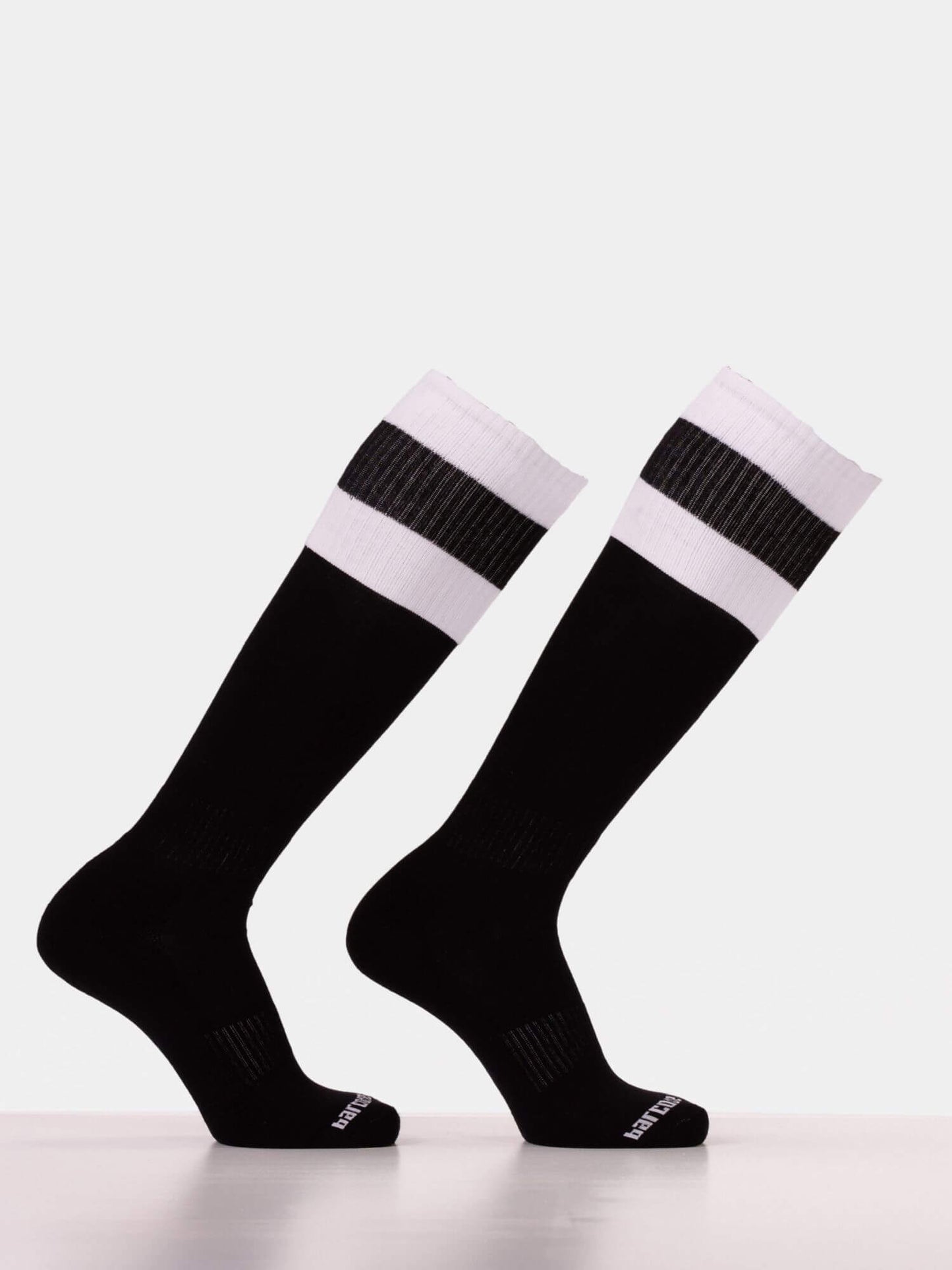 A pair of black knee-high athletic socks with two white horizontal stripes near the ribbed cuffs, displayed on invisible forms against a light gray background.