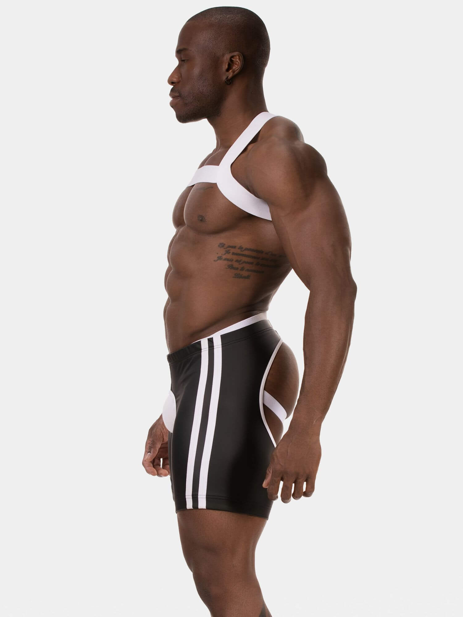A muscular man shown in profile wearing black athletic shorts with white side stripes and a white harness-style top against a light gray studio background.