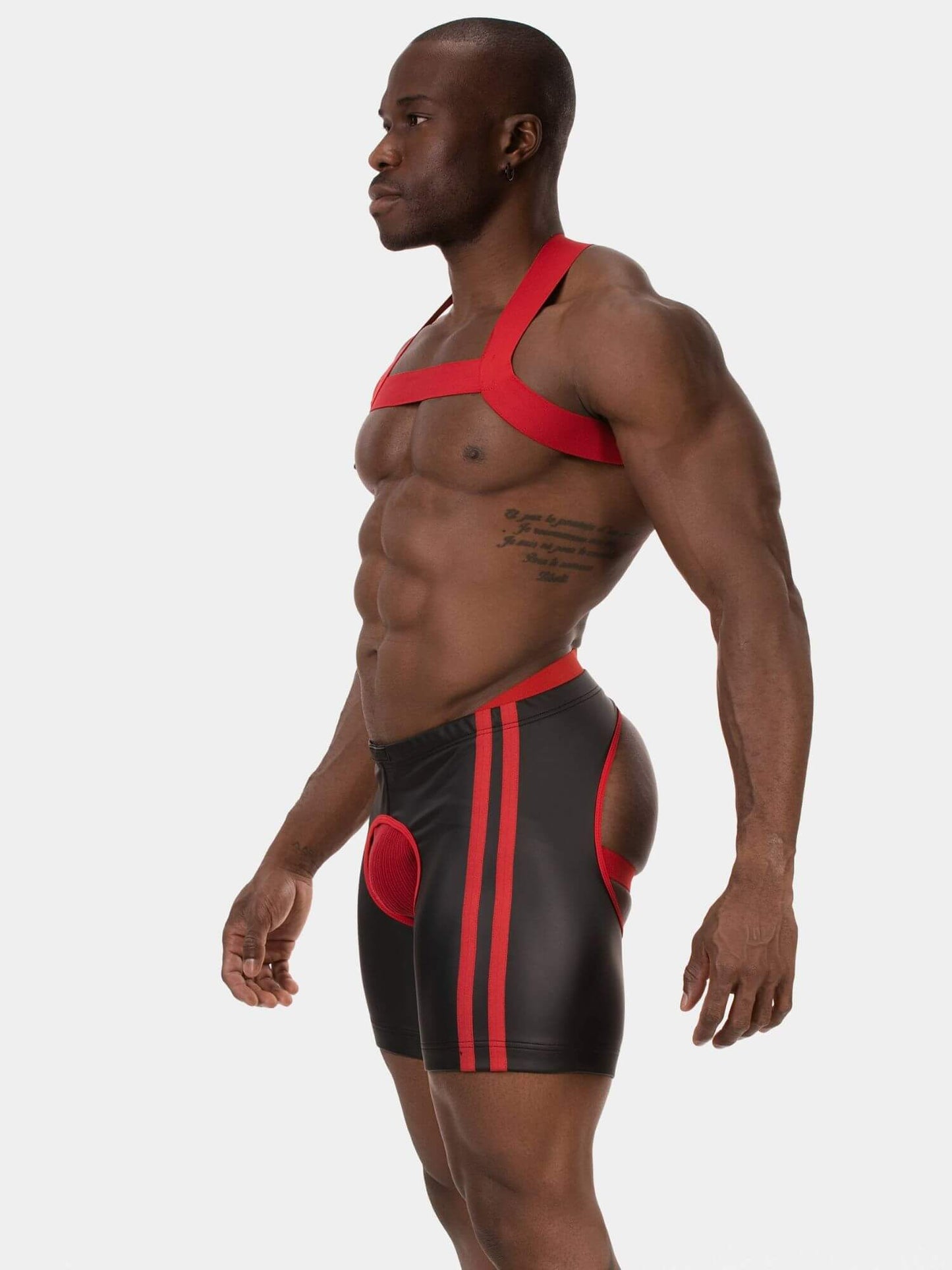 A muscular man shown in profile wearing a red and black athletic harness-style top and matching black shorts with red side panels and stripes, photographed against a light gray studio background.