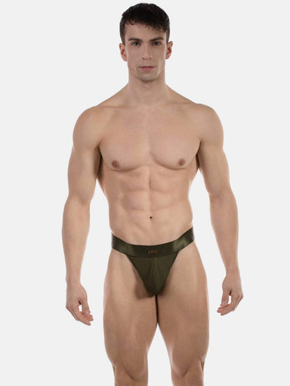 A muscular man modeling a low-rise, semi-sheer olive green jockstrap against a plain light gray background.