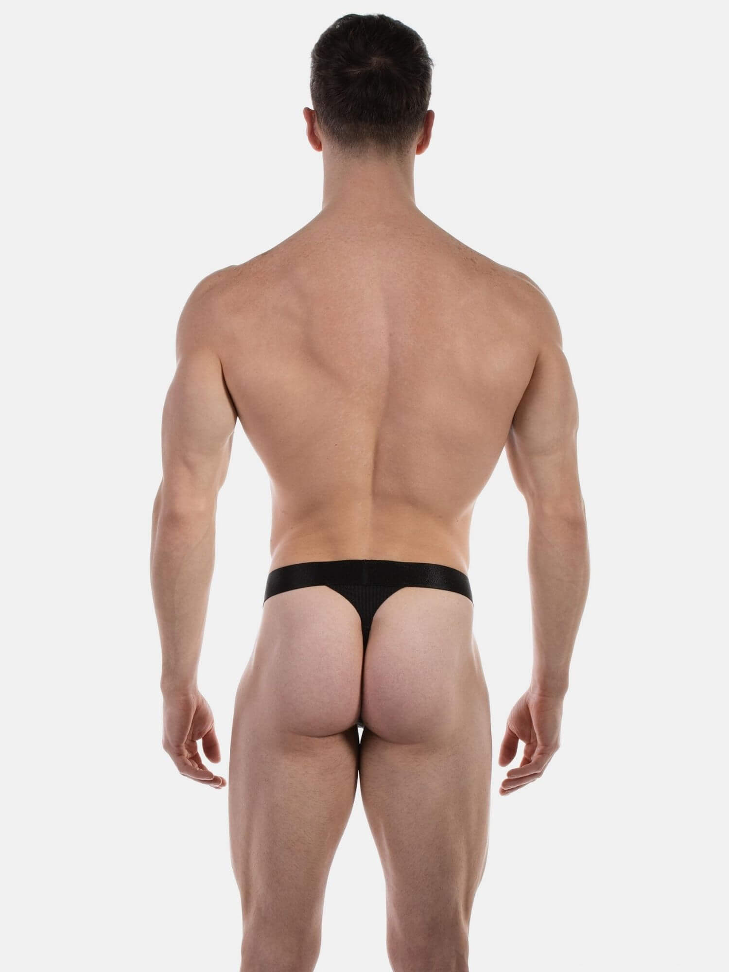 Rear view of a muscular man wearing a black thong against a plain light gray studio background.