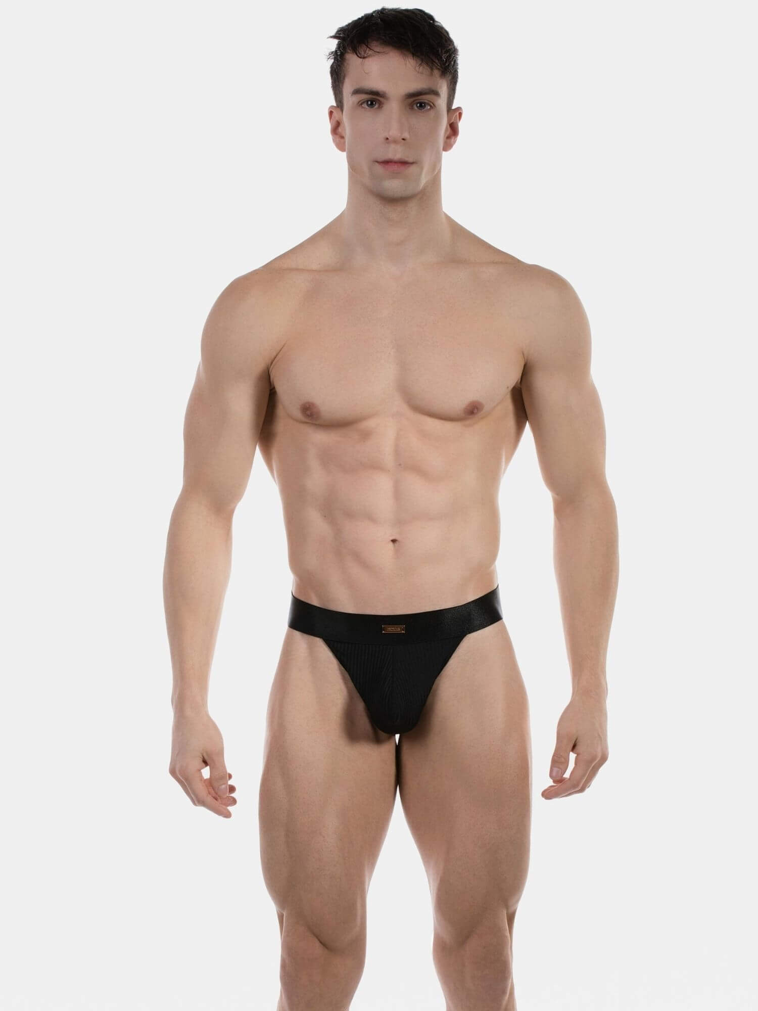 A muscular man modeling a black men's low-rise brief against a plain light gray studio background.