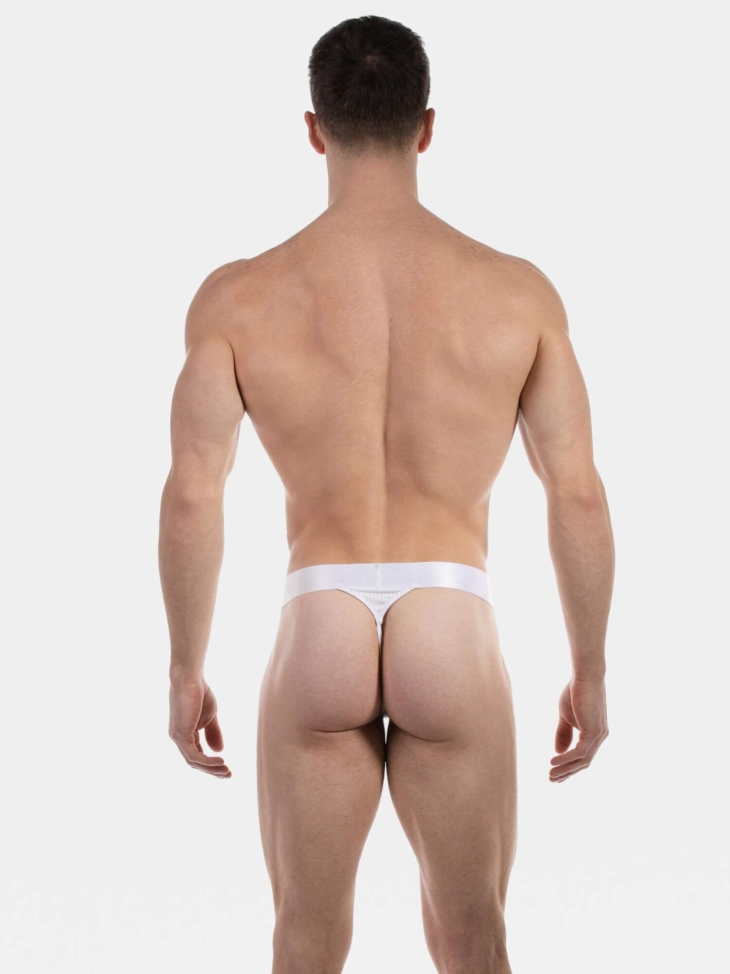 Rear view of a muscular man wearing a white thong against a light gray studio background.