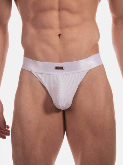 A close-up of a male model's lower torso wearing a white ribbed thong with a small gold rectangular logo plaque on the front waistband, set against a plain white studio background.