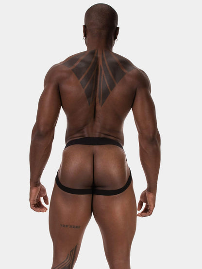 Rear view of a muscular man with tattoos wearing black men's briefs against a light gray studio background.
