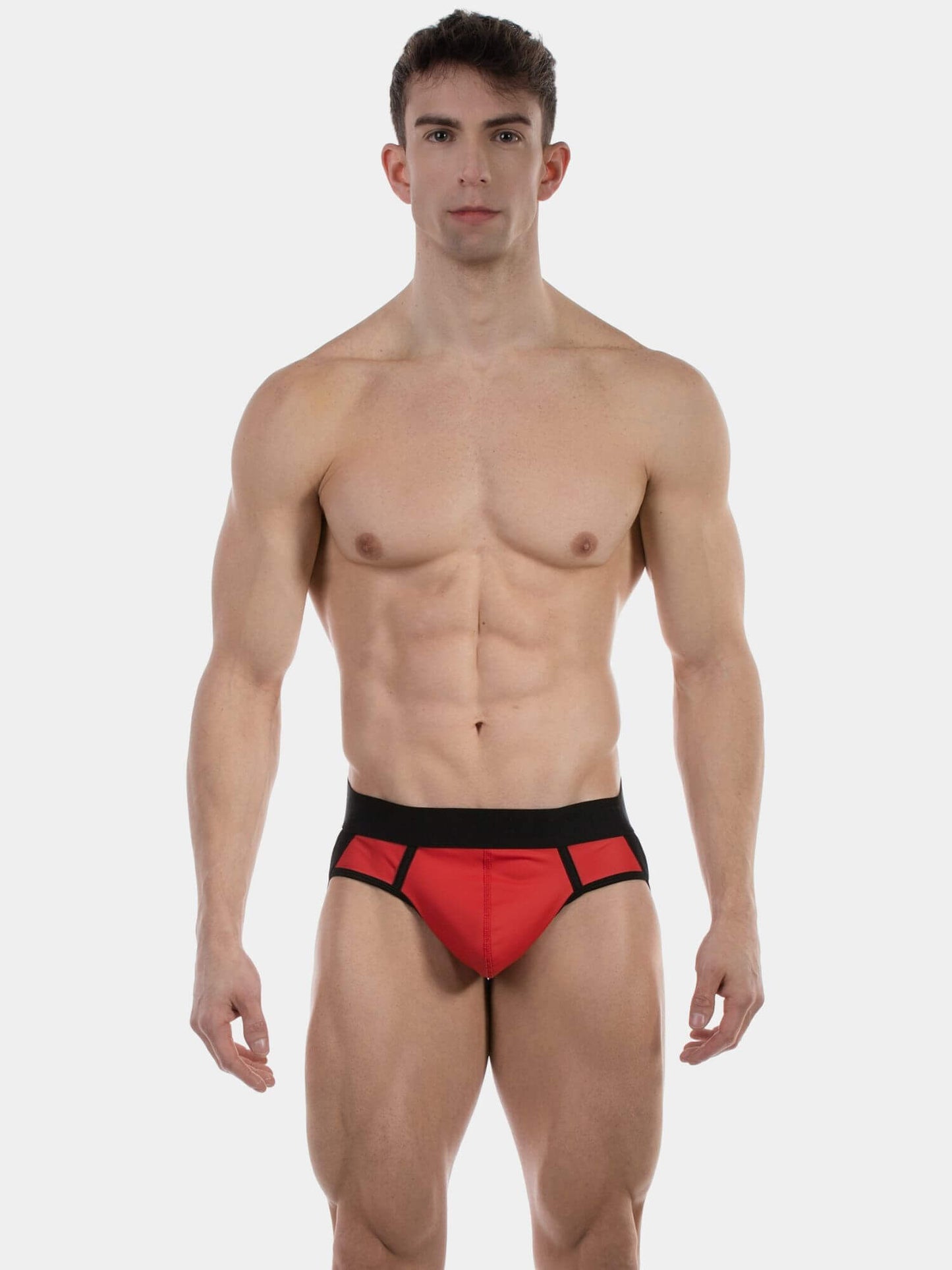 A muscular man modeling a pair of men's briefs in red with a black waistband and black trim, shot against a solid light gray background.