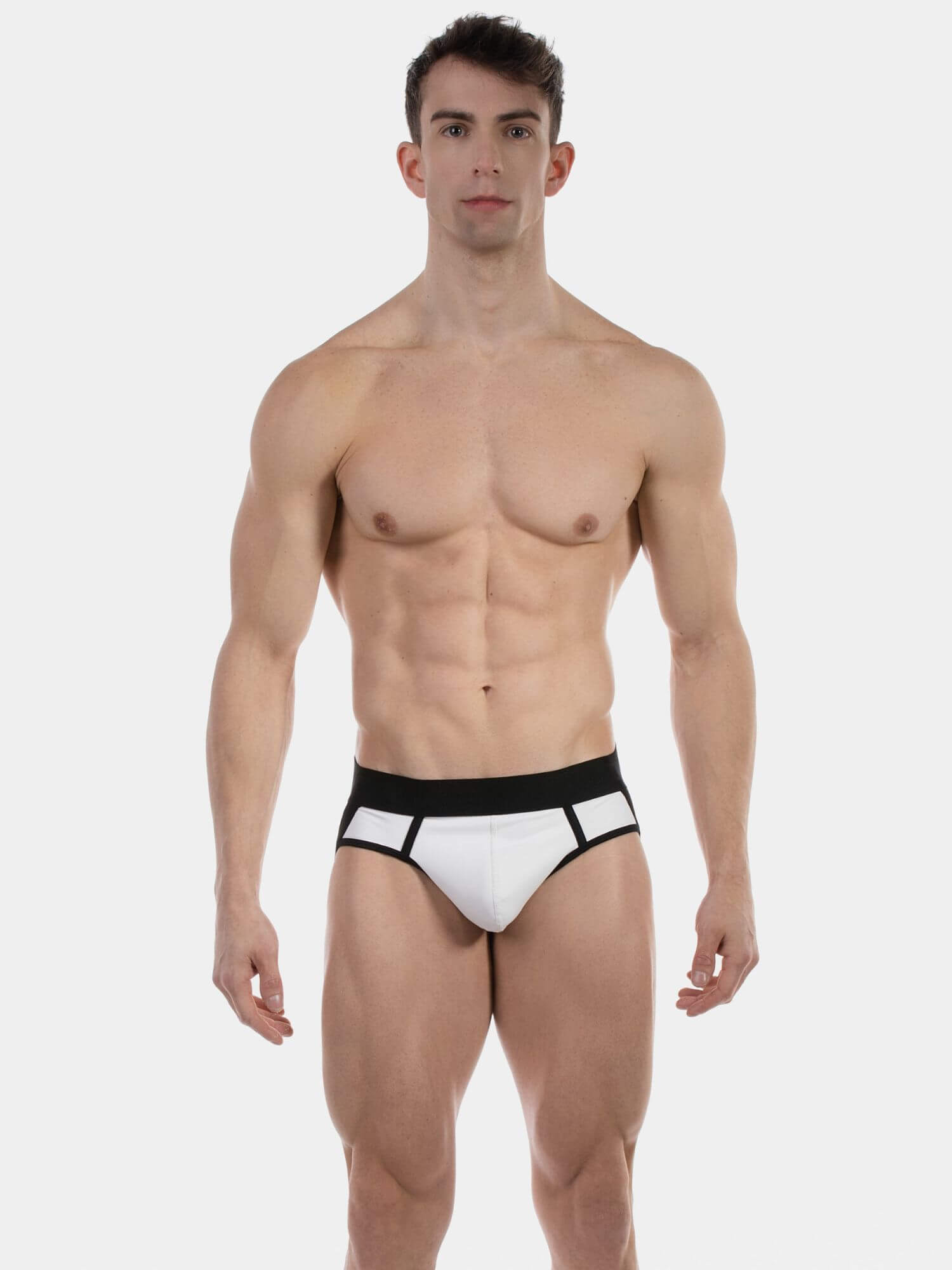 A muscular male model wearing white briefs with a black waistband and black side trim, standing against a light gray studio background.