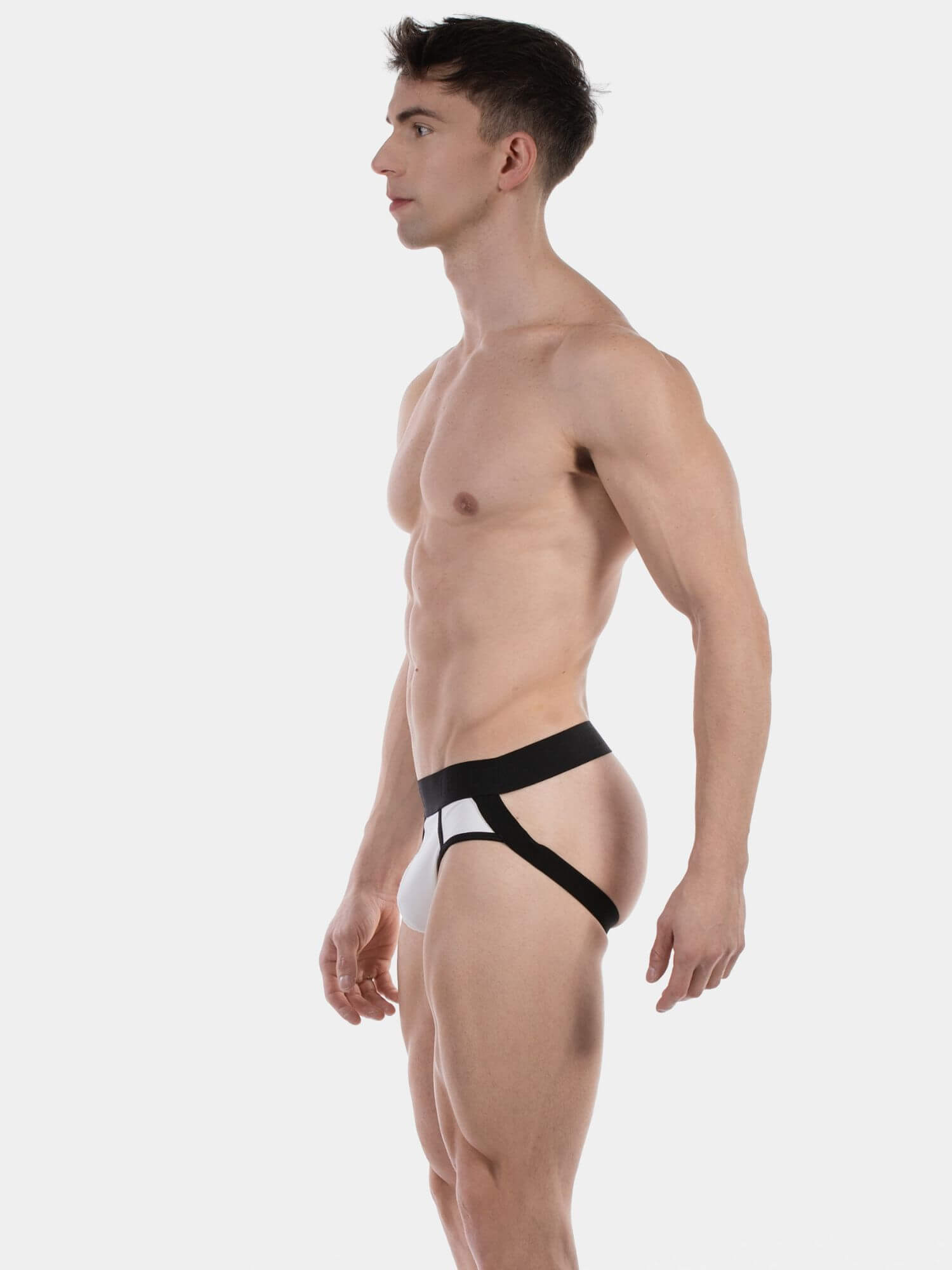 A muscular man shown in profile wearing a black and white jockstrap, photographed against a solid light gray background.