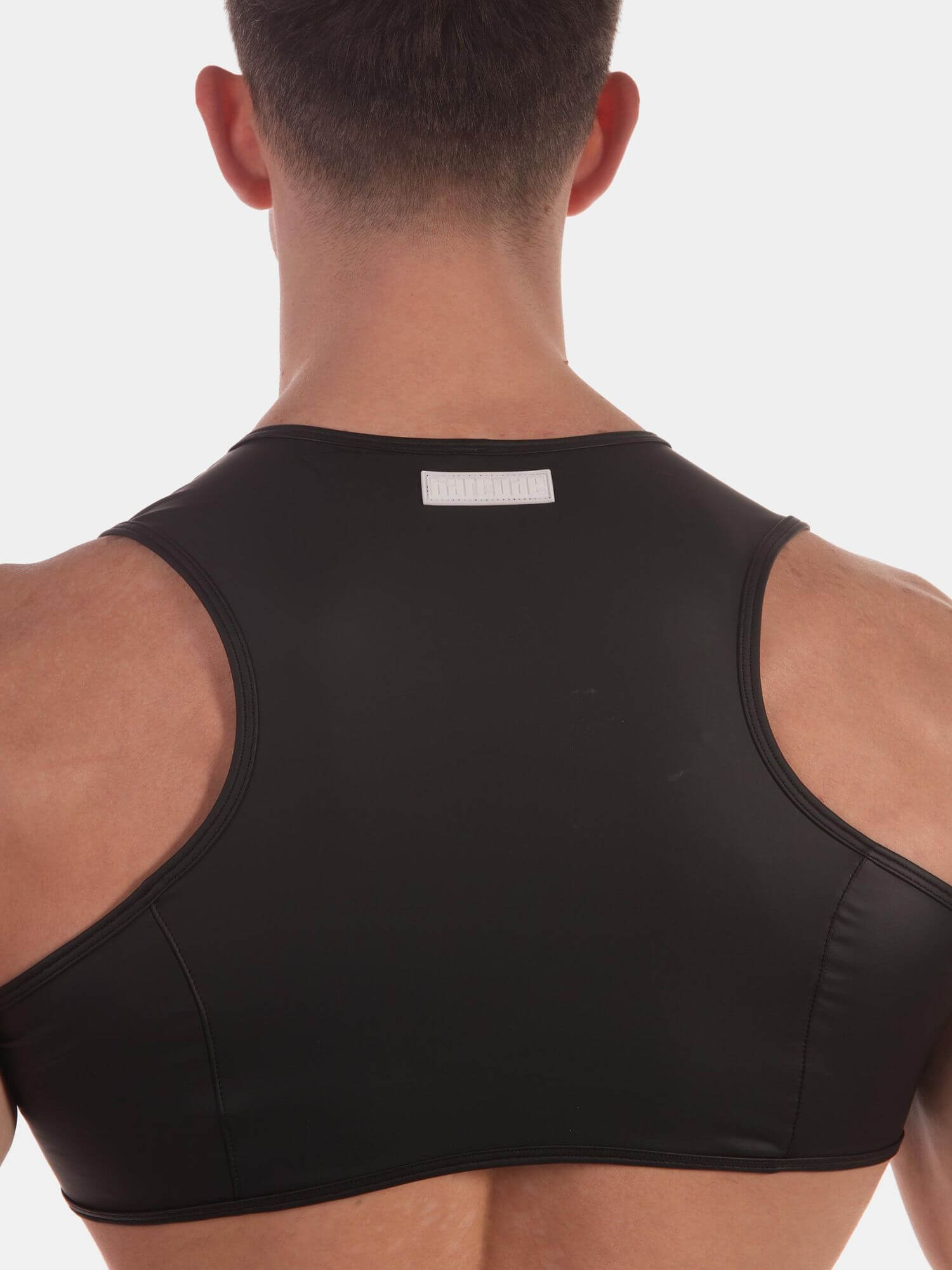 Rear view of a man wearing a black athletic tank top or sports bra against a light gray studio background.