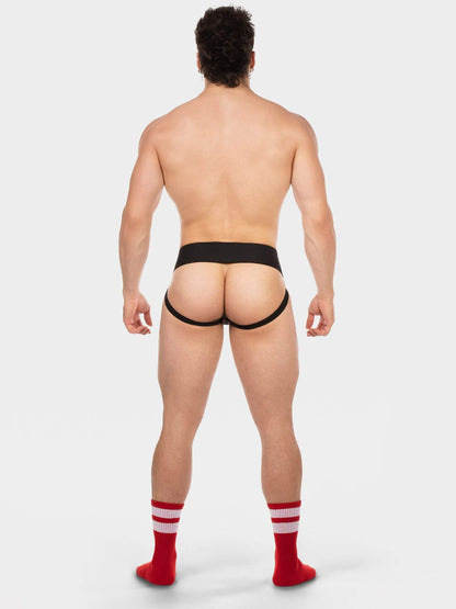 A muscular man is shown from behind wearing black men's briefs and red crew socks with white stripes, standing against a light gray studio background.
