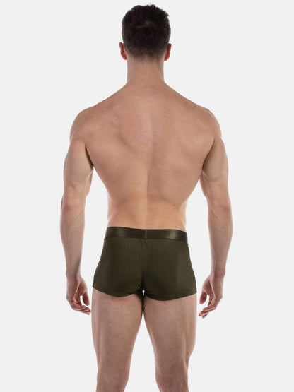 Rear view of a muscular man wearing olive green textured boxer briefs against a light gray studio background.