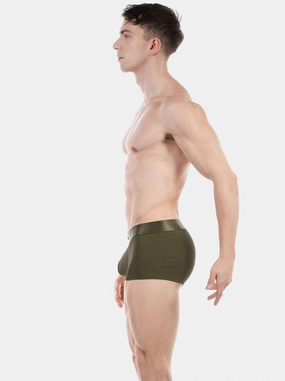 A man shown in side profile wearing olive green ribbed boxer briefs against a plain light gray studio background.