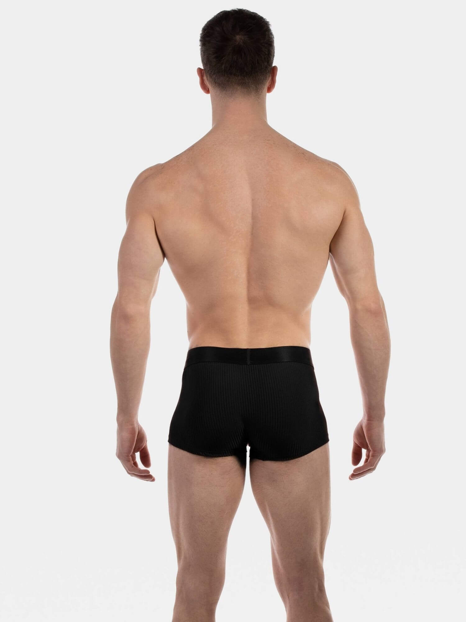 A man viewed from behind wearing black boxer briefs against a clean white studio background.