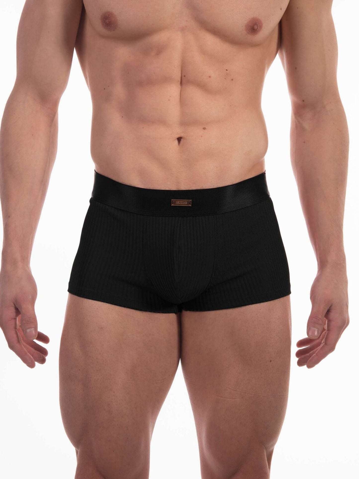 A male model wearing black ribbed boxer briefs against a plain white studio background.