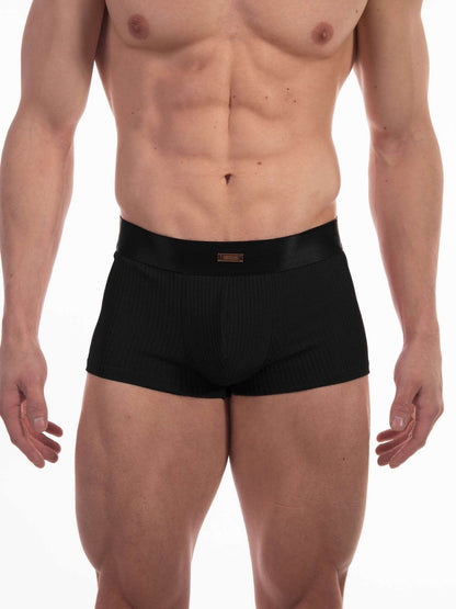 A male model wearing black ribbed boxer briefs against a plain white studio background.
