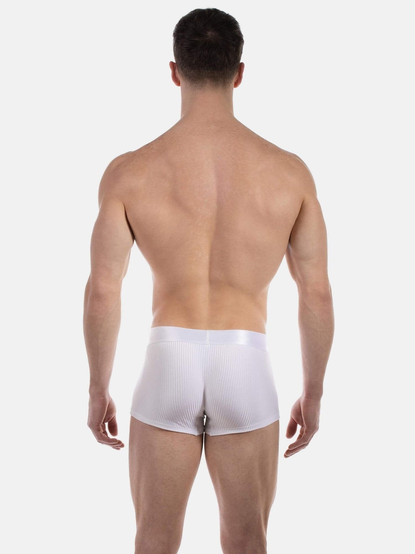 A man viewed from the back wearing white ribbed boxer briefs against a light gray studio background.
