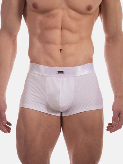 A close-up of a male model's lower torso wearing white ribbed boxer briefs against a plain light gray studio background.