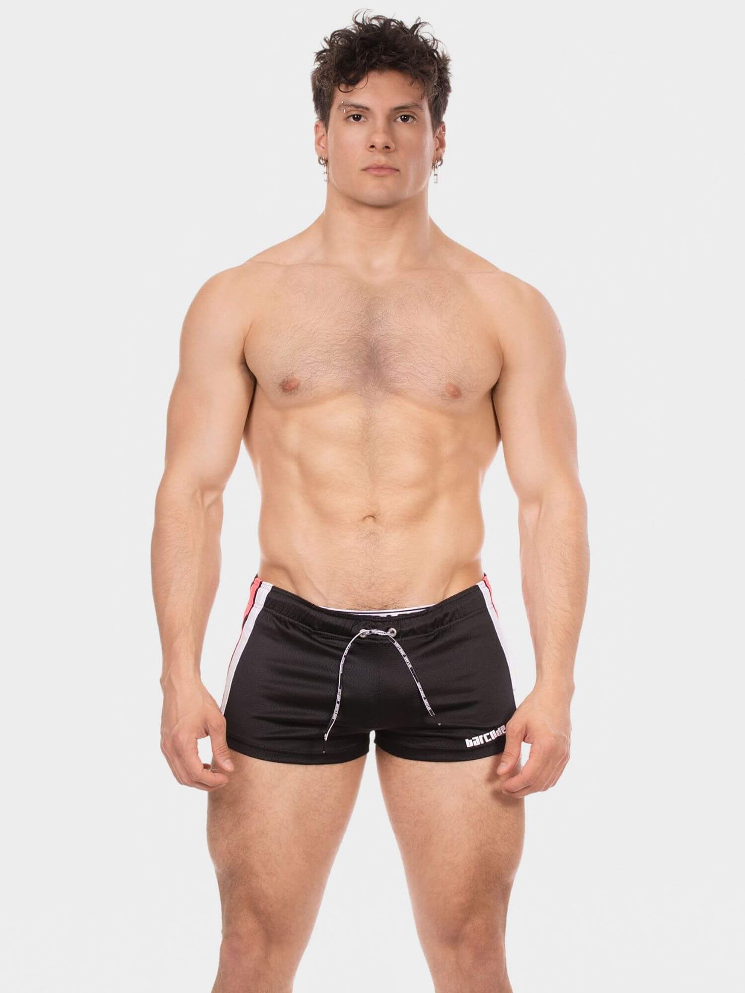 A shirtless man modeling black athletic shorts with white and red side stripes and a white drawstring, photographed against a light gray studio background.
