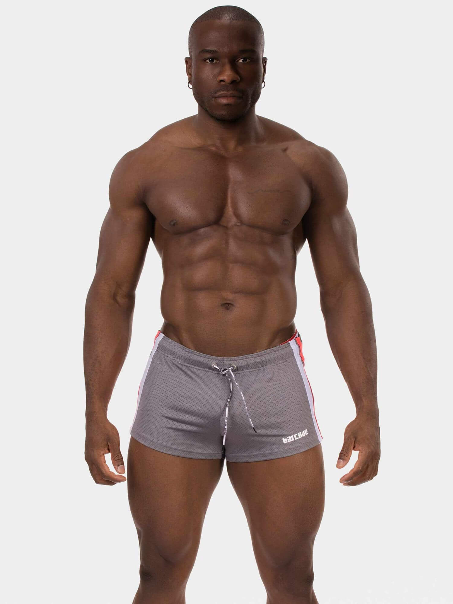 A muscular man wearing gray athletic shorts with white and red side stripes, standing against a light gray background.