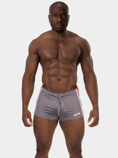 A muscular man wearing gray athletic shorts with white and red side stripes, standing against a light gray background.
