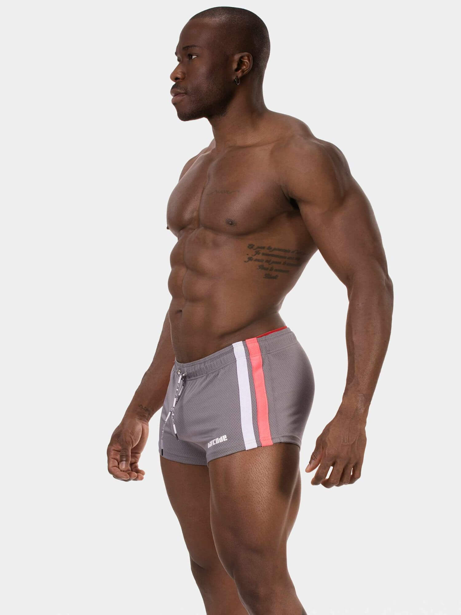 A muscular man shown from the waist up in side profile, wearing gray athletic shorts with a vertical white stripe and a pink accent stripe on the side, against a light gray studio background.