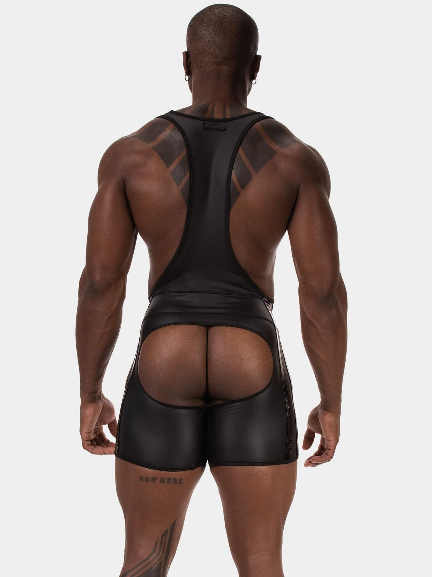 Rear view of a muscular man wearing a black athletic singlet and matching black shorts against a light gray studio background.