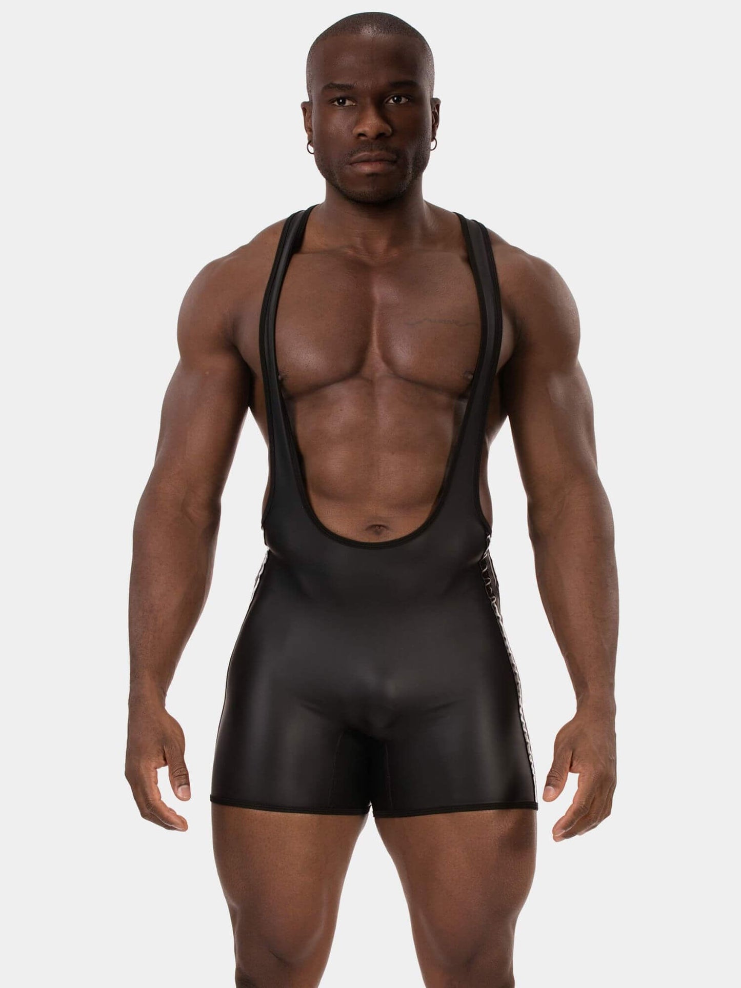 A muscular man modeling a black, form-fitting bib-style shorty with wide shoulder straps against a light gray studio background.