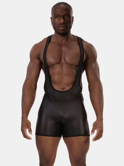 A muscular man modeling a black, form-fitting bib-style shorty with wide shoulder straps against a light gray studio background.