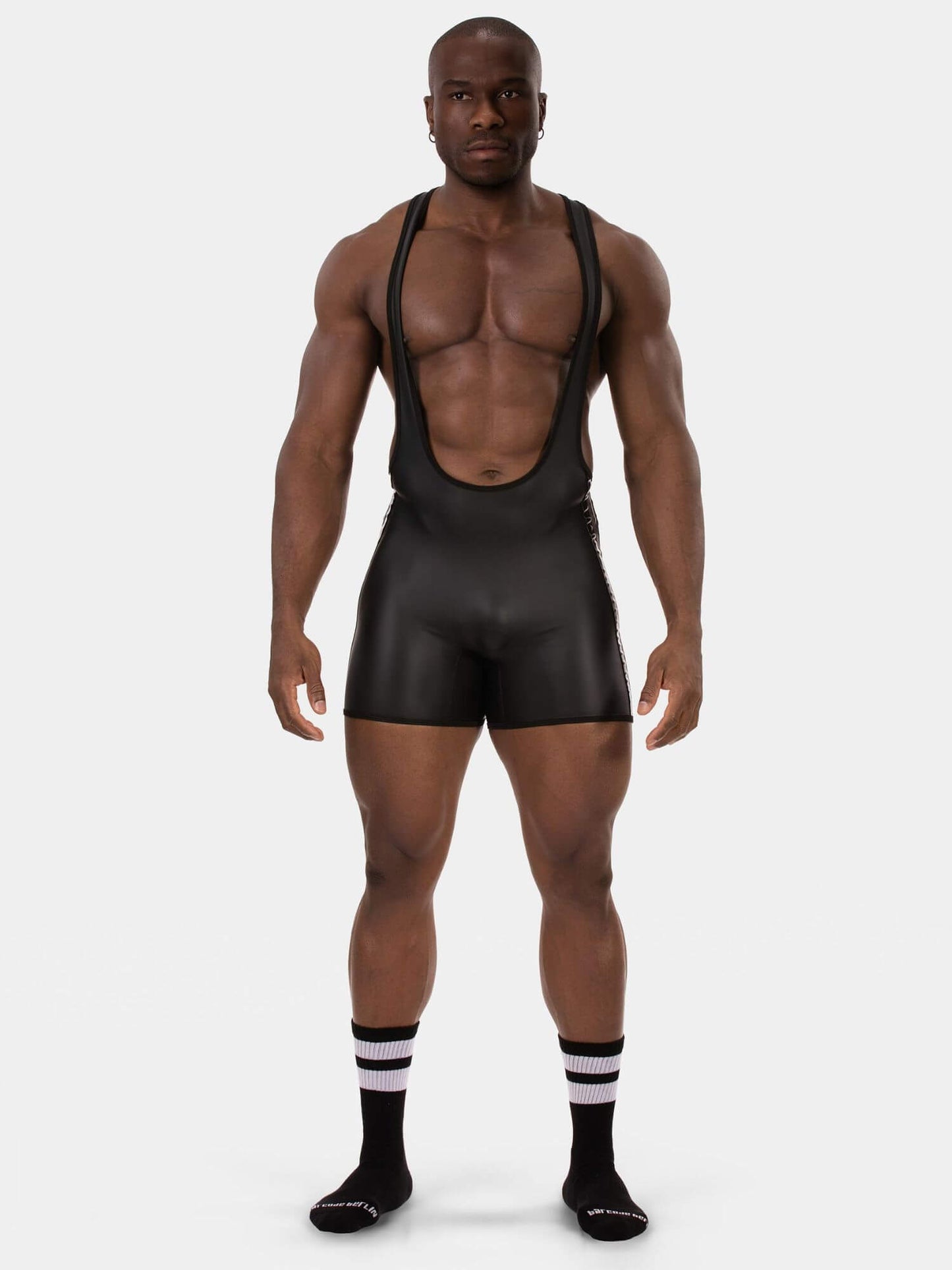 A muscular male model wearing a black wrestling singlet paired with black and white socks against a solid light gray background.