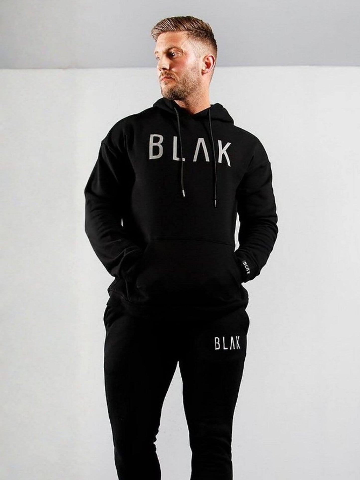 Man wearing a black hoodie and pants with 'BLAK' branding on a white background