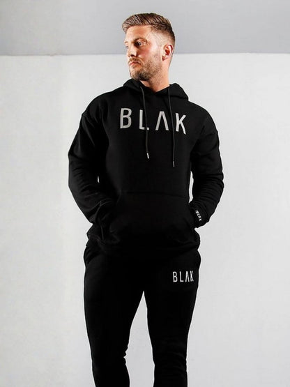 Man wearing a black hoodie and pants with 'BLAK' branding on a white background