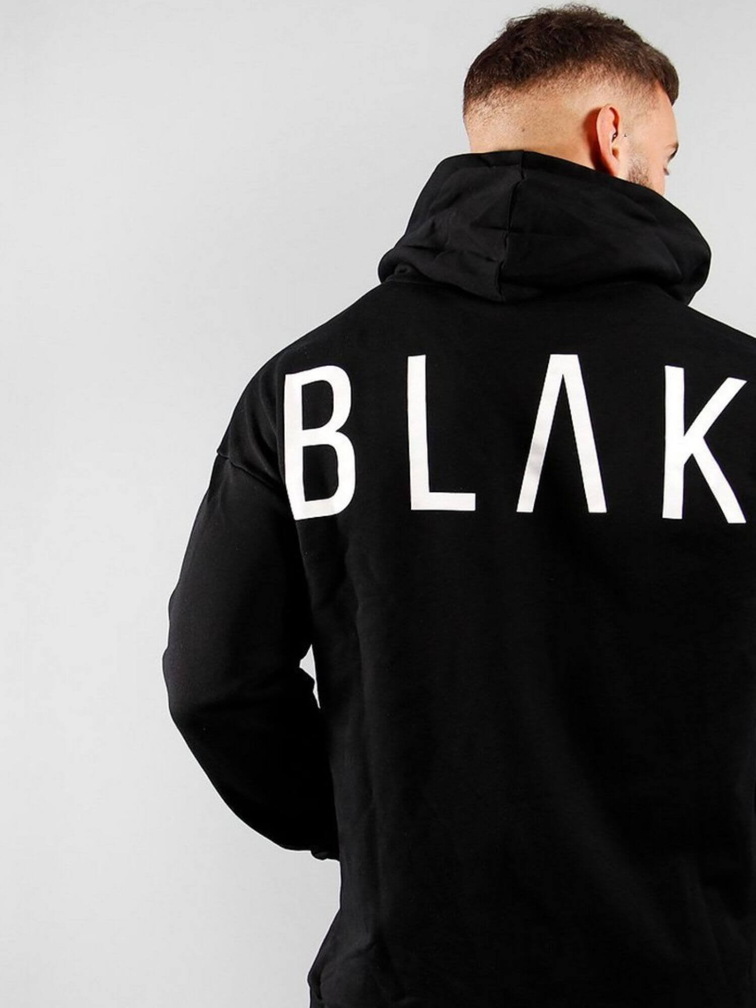 Person wearing a black hoodie with 'BLAK' printed on the back against a light gray background