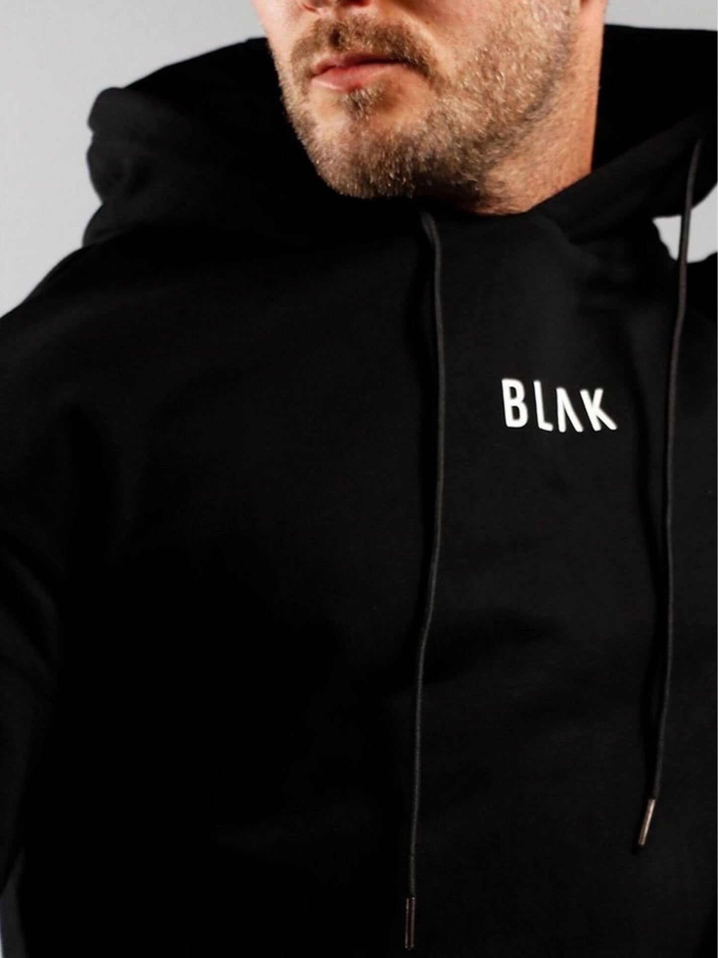 Person wearing a black hoodie with 'BLAK' logo on a plain background