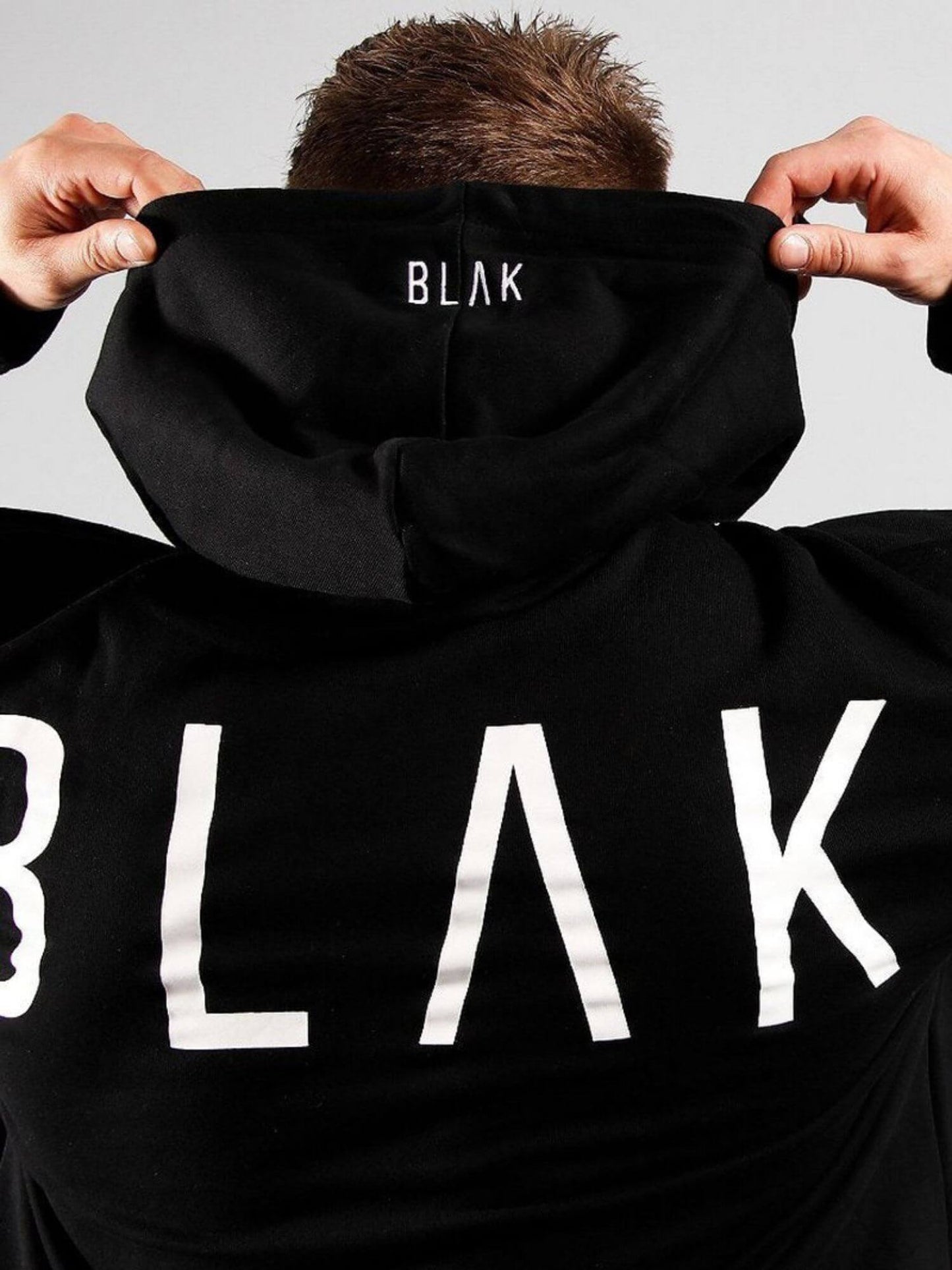 Person wearing a black hoodie with 'BLAK' branding on a plain background