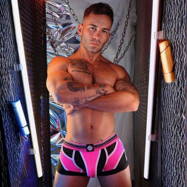 Man wearing pink and black patterned Breedwell Circuit Breaker underwear in a room with chains and a mirror.