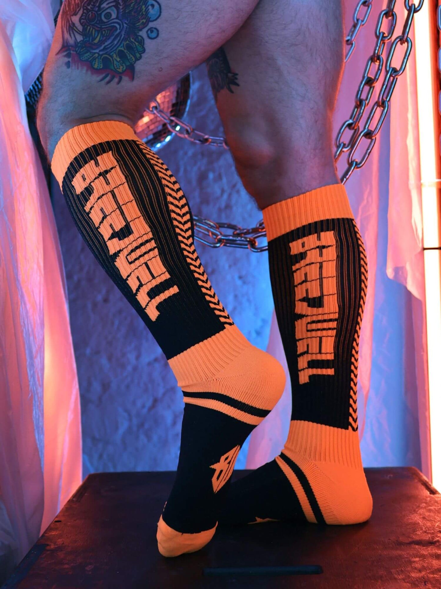 Orange and black socks with visible branding on a person's legs against a colorful background.