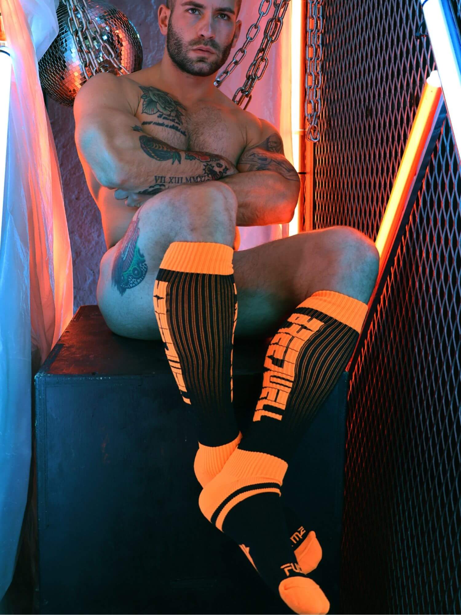 Man wearing black and orange socks with visible branding in a dimly lit room.