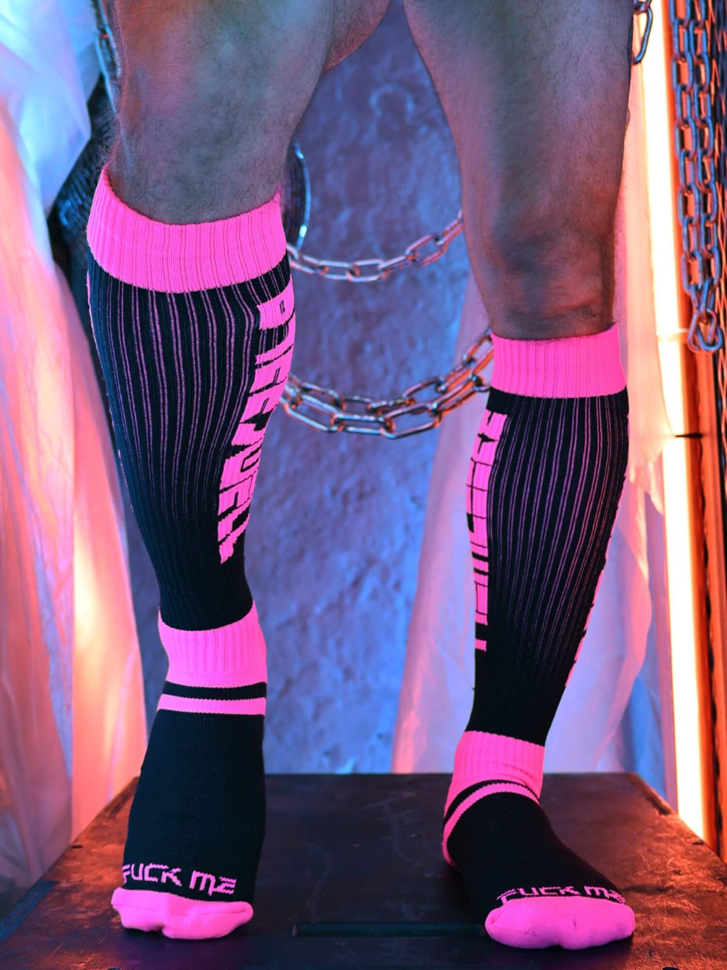 Person wearing black and pink  socks with visible text against a textured wall.