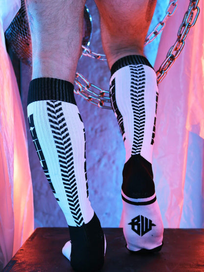 Person wearing black and white knee-high socks with a pattern, standing on a wooden floor with a colorful curtain background.