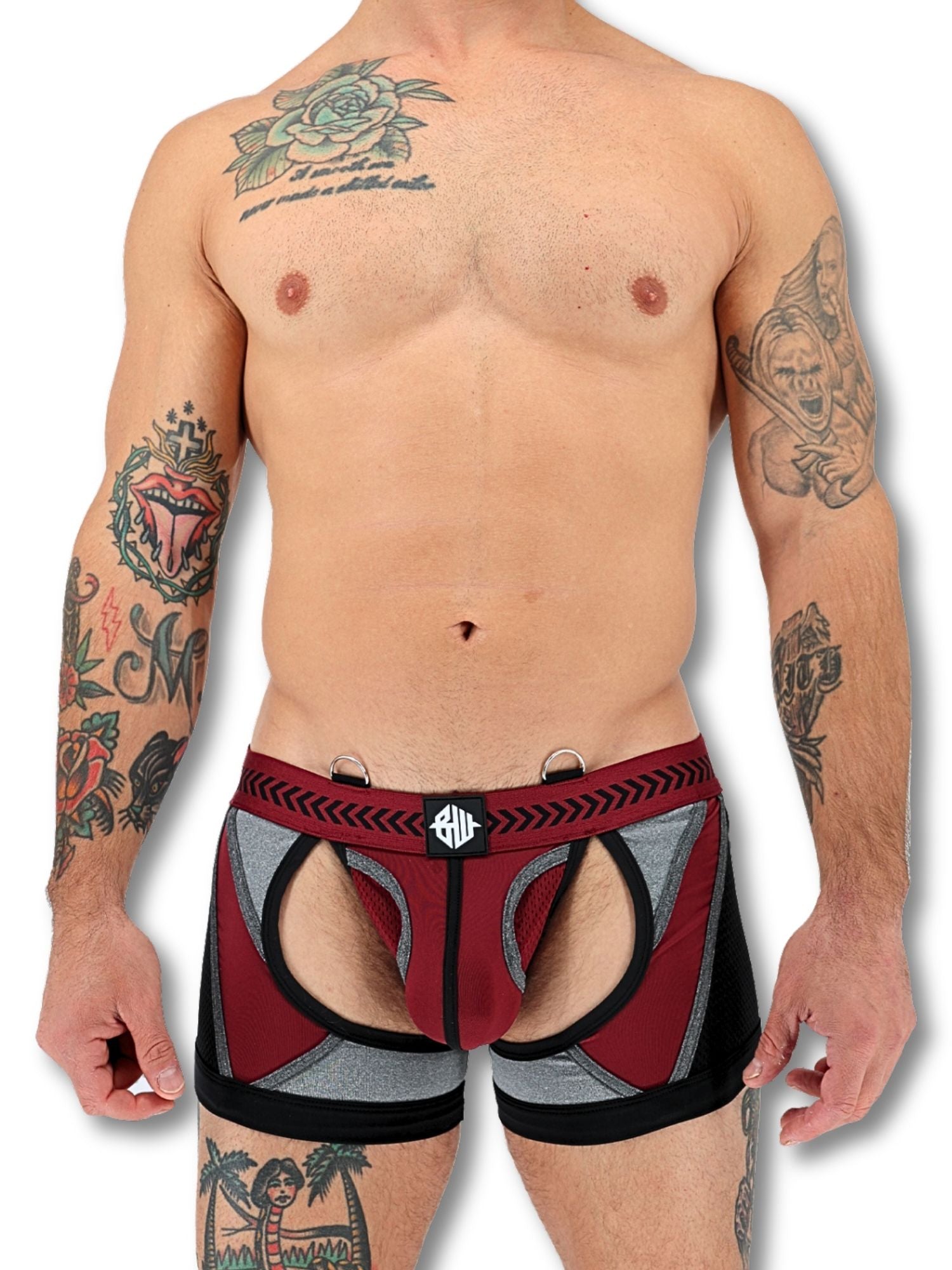 Man wearing patterned underwear with tattoos on arms and chest against a white background