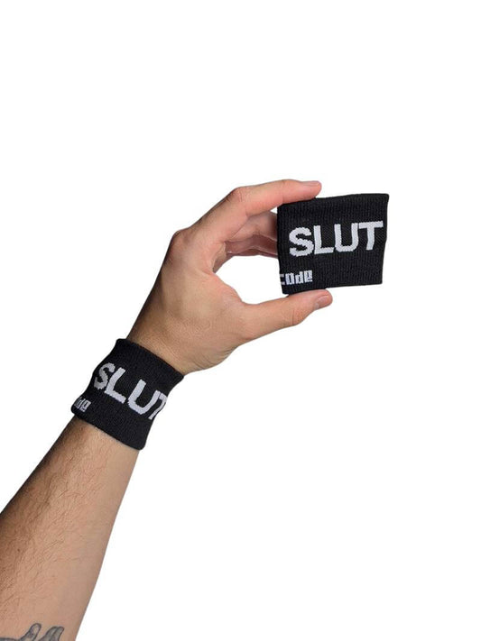 A hand holding two black wristbands with the text 'slut' written in white lettering and a black stripe design.