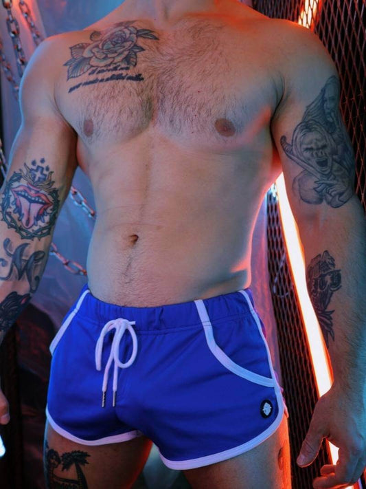 Man wearing blue swim shorts with tattoos on arms and chest.